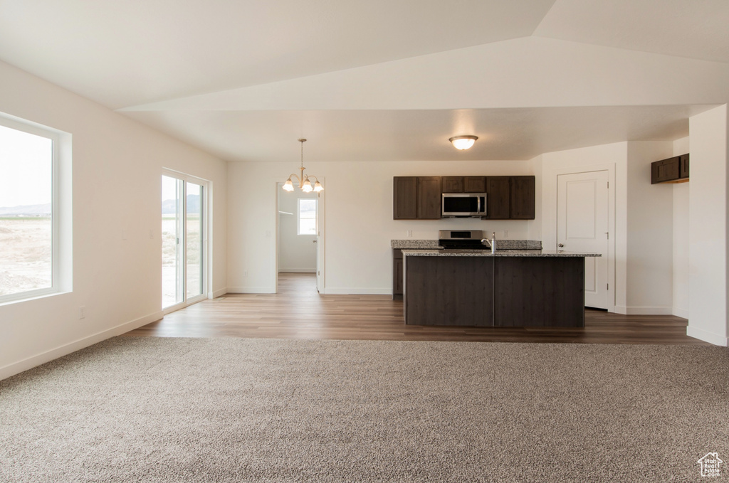 Kitchen with appliances with stainless steel finishes, vaulted ceiling, dark brown cabinets, hardwood / wood-style floors, and a notable chandelier