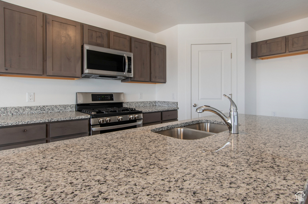 Kitchen featuring stainless steel appliances, light stone counters, dark brown cabinetry, and sink