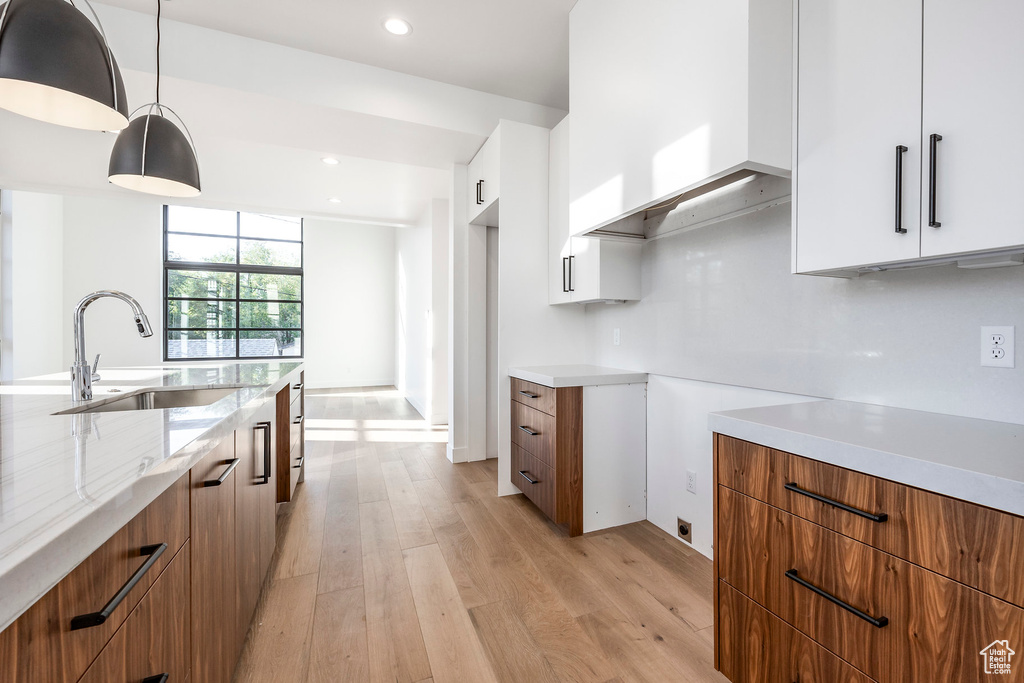 Kitchen featuring light hardwood / wood-style flooring, hanging light fixtures, sink, and white cabinets