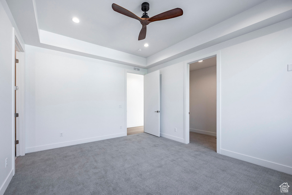 Unfurnished bedroom featuring a spacious closet, ceiling fan, carpet flooring, and a tray ceiling