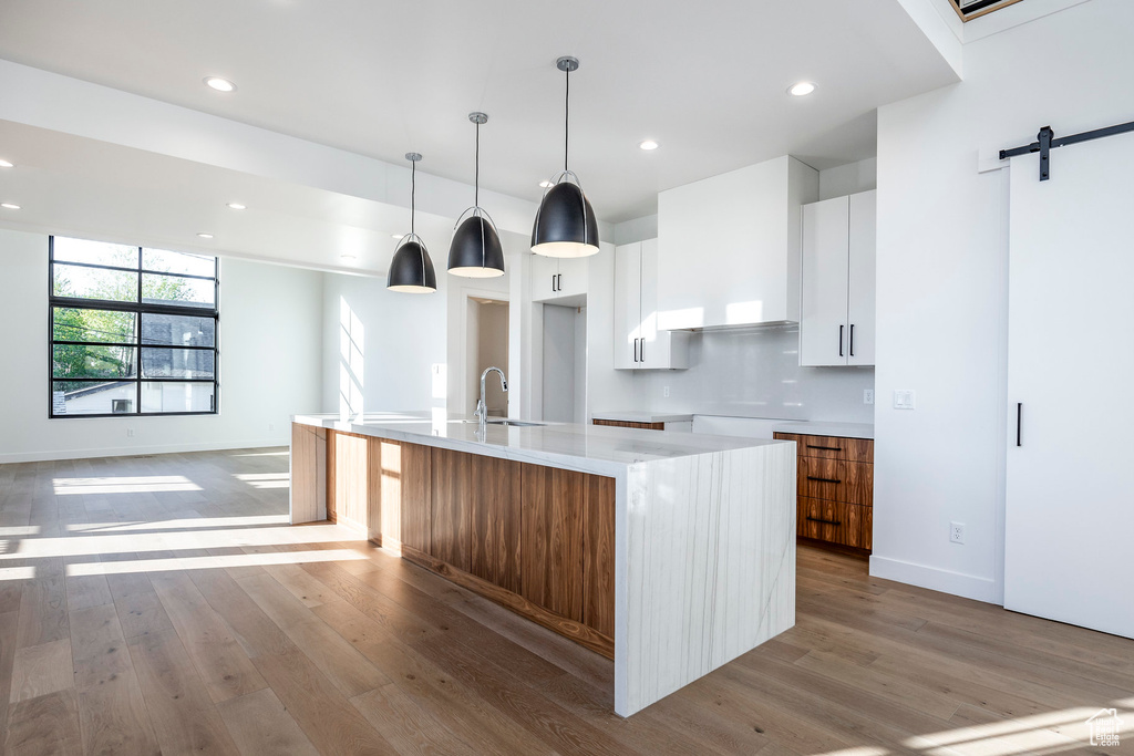 Kitchen featuring a barn door, hanging light fixtures, white cabinetry, light hardwood / wood-style floors, and a kitchen island with sink