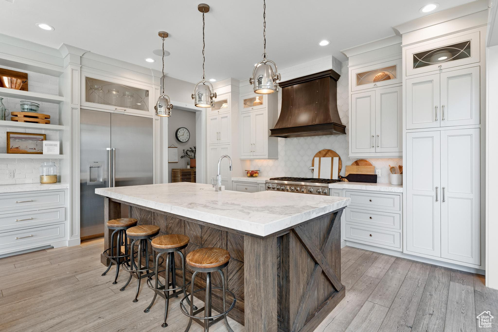 Kitchen featuring a center island with sink, decorative backsplash, premium range hood, and stainless steel appliances