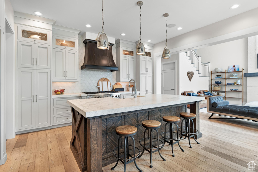 Kitchen with light hardwood / wood-style floors, light stone countertops, hanging light fixtures, and a center island with sink