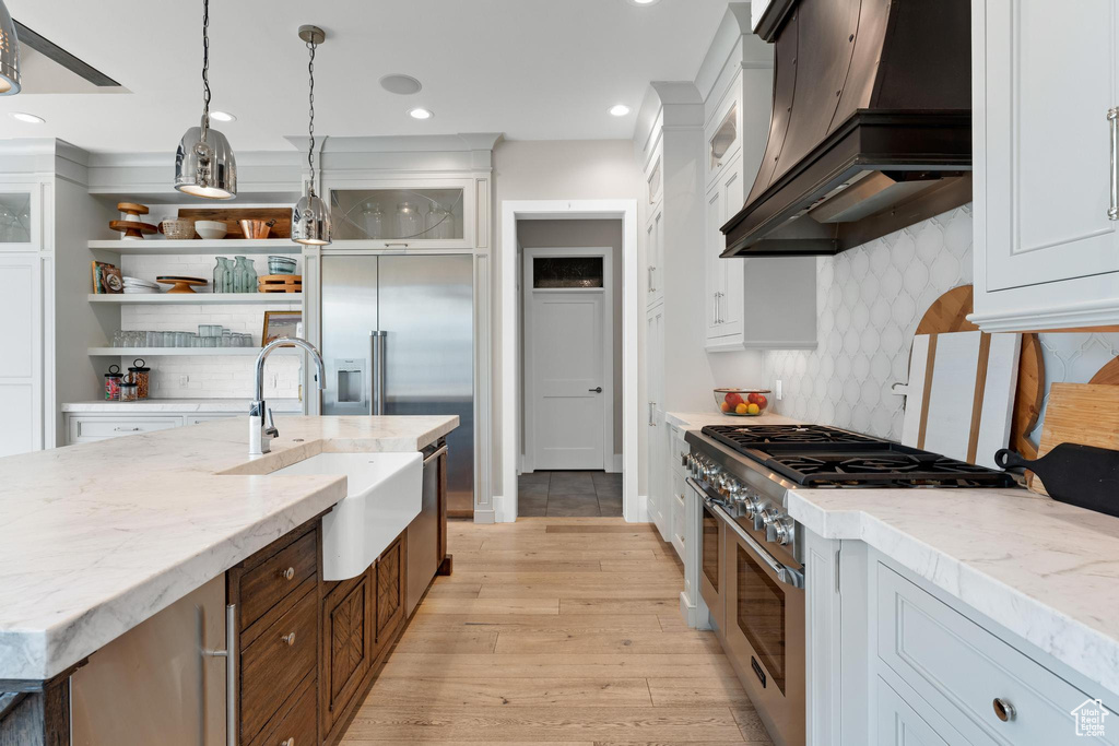 Kitchen featuring sink, decorative light fixtures, custom exhaust hood, appliances with stainless steel finishes, and light hardwood / wood-style floors