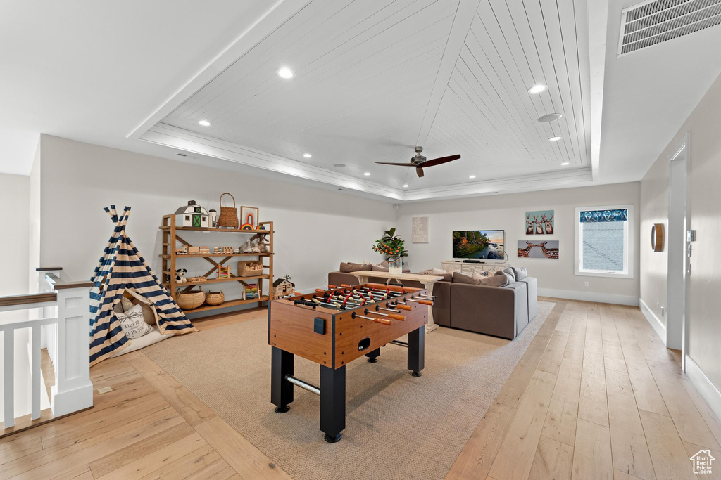 Rec room with light hardwood / wood-style floors, a tray ceiling, and ceiling fan