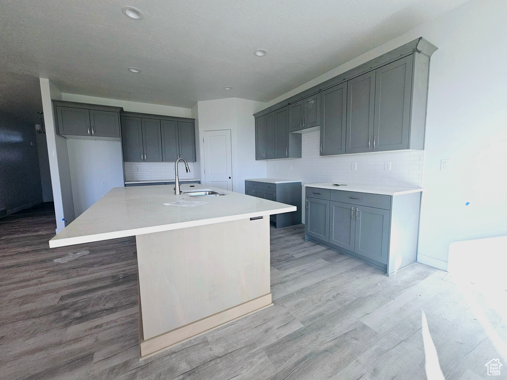 Kitchen with light hardwood / wood-style flooring, sink, backsplash, and a kitchen island with sink