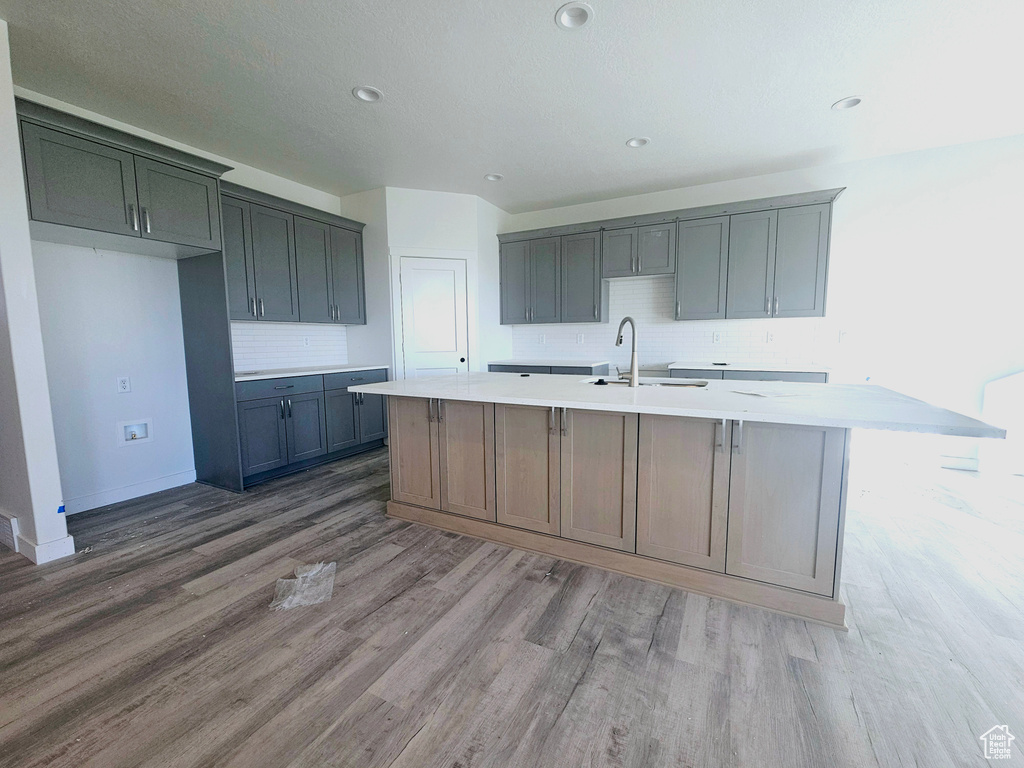 Kitchen with hardwood / wood-style flooring, decorative backsplash, sink, and an island with sink