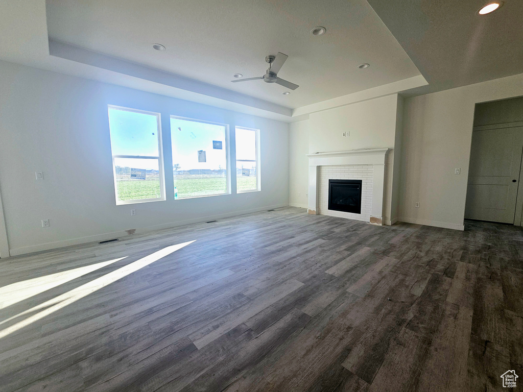 Unfurnished living room featuring a raised ceiling, dark hardwood / wood-style flooring, and a brick fireplace