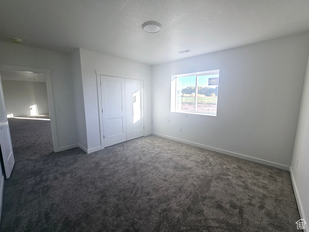 Unfurnished bedroom with a closet, a textured ceiling, and dark carpet