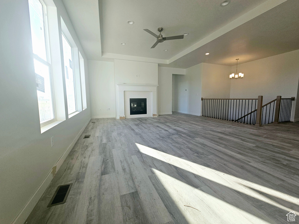 Unfurnished living room with a raised ceiling, light wood-type flooring, and ceiling fan with notable chandelier