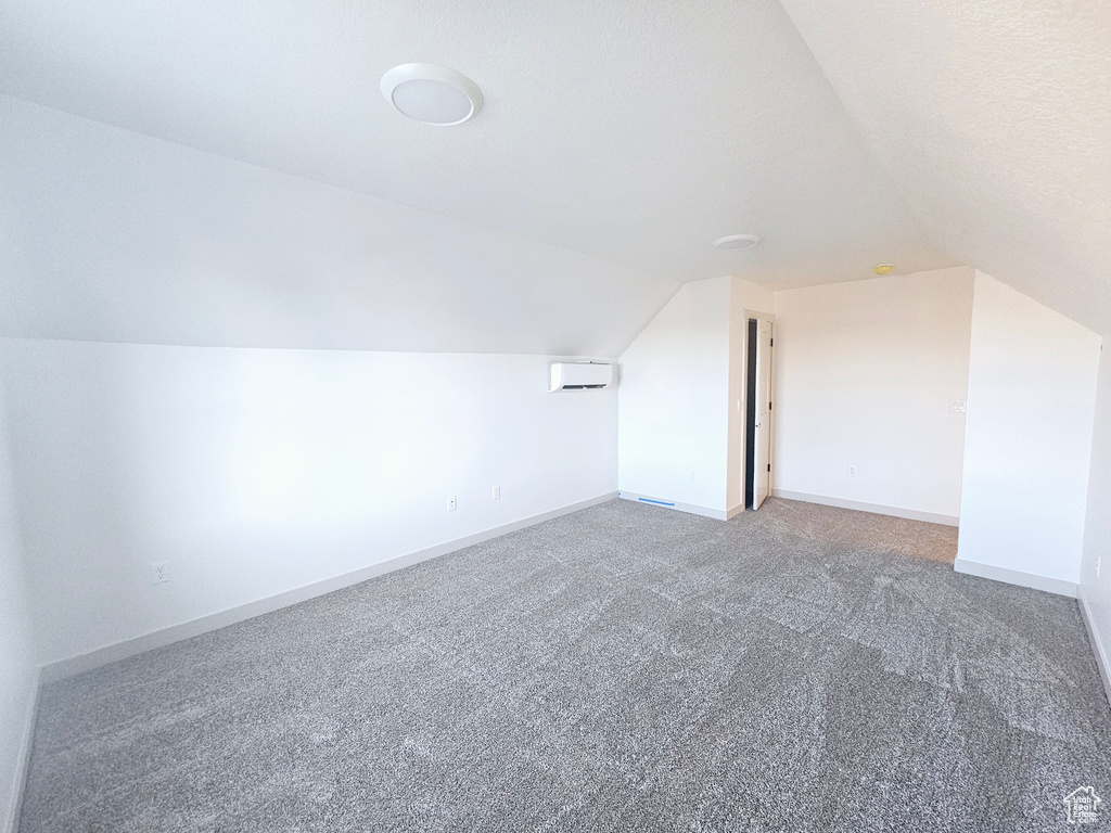 Additional living space with a textured ceiling, carpet flooring, lofted ceiling, and a wall unit AC