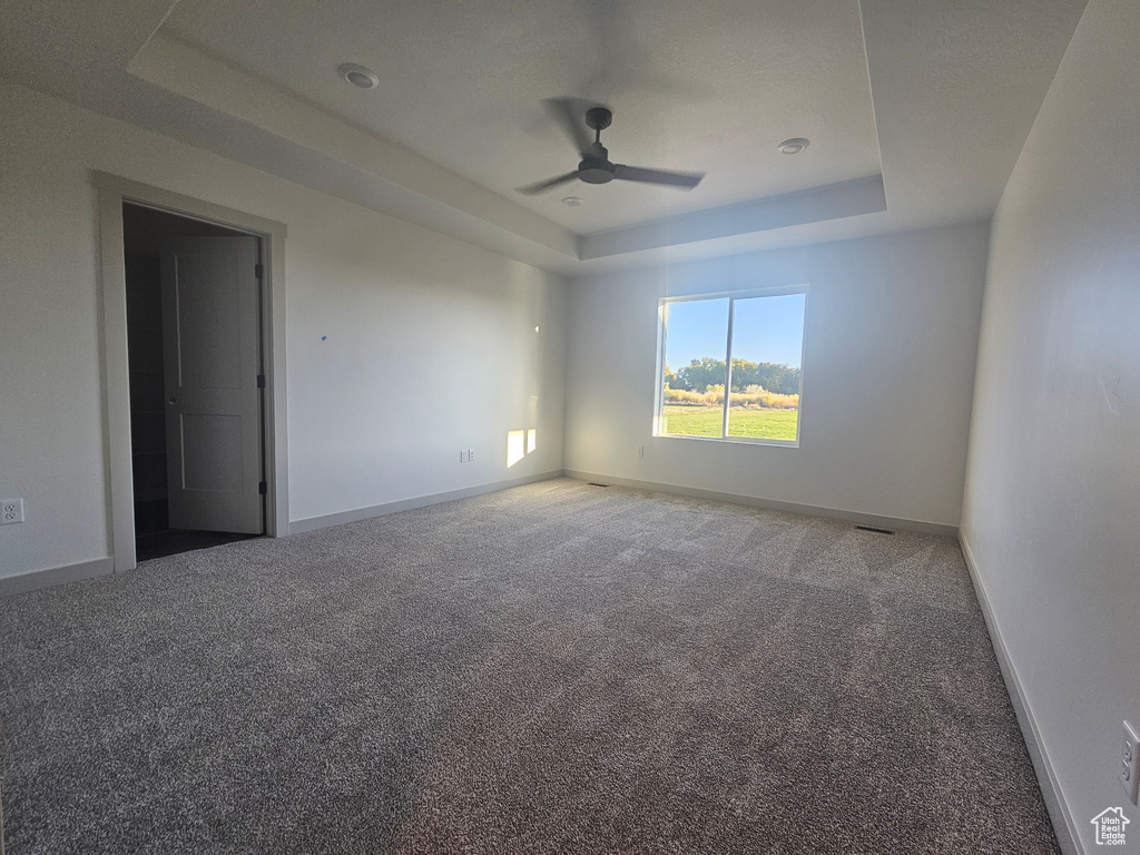 Carpeted empty room featuring ceiling fan and a raised ceiling