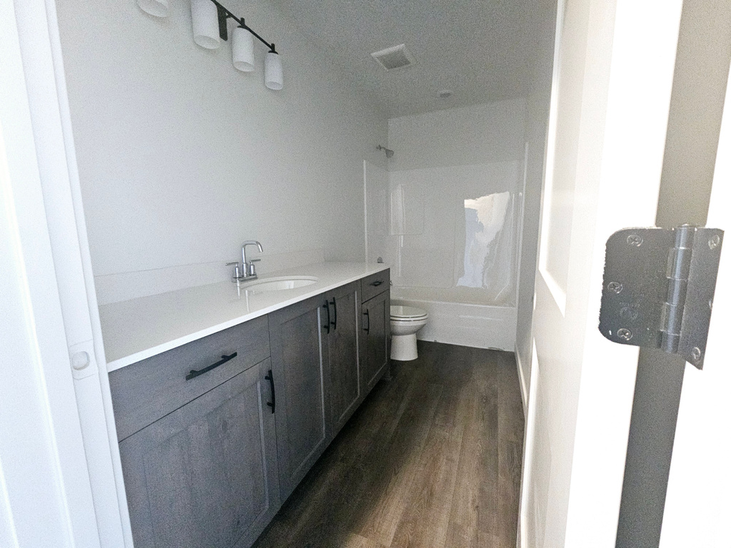 Full bathroom with bathing tub / shower combination, a textured ceiling, toilet, vanity, and hardwood / wood-style flooring