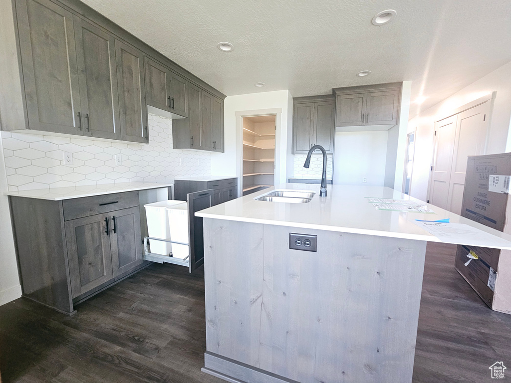 Kitchen with dark hardwood / wood-style floors, a center island with sink, sink, a textured ceiling, and tasteful backsplash