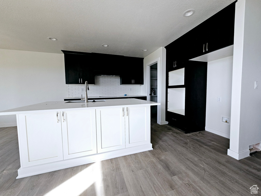 Kitchen with hardwood / wood-style floors, sink, a kitchen island with sink, and decorative backsplash