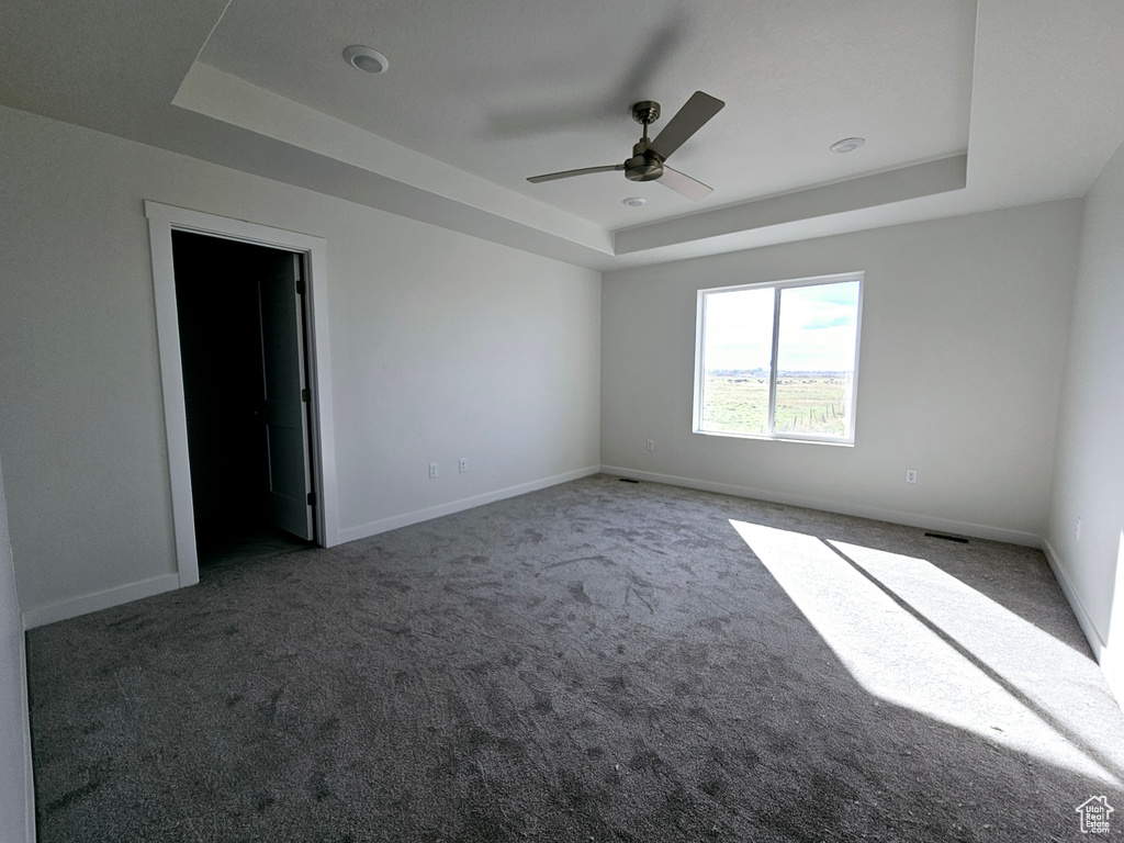 Carpeted empty room with ceiling fan and a raised ceiling