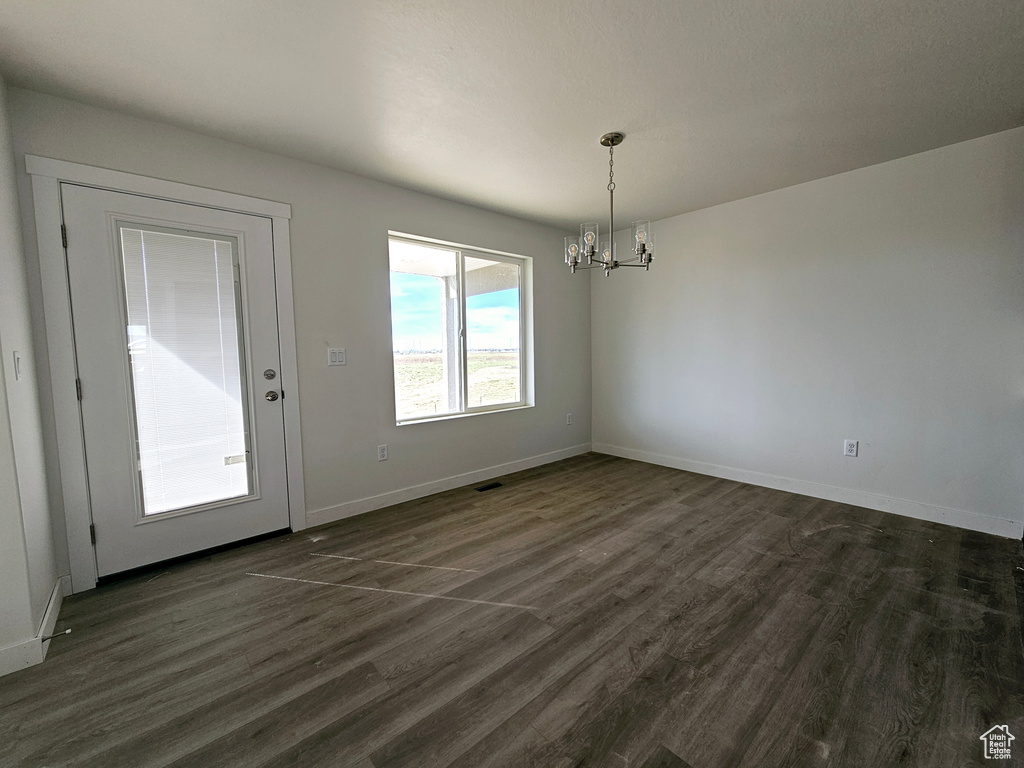 Unfurnished dining area with dark wood-type flooring and a chandelier