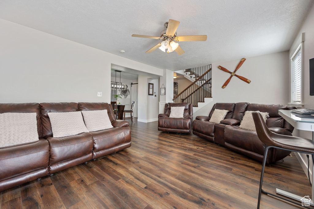 Living room with dark wood-type flooring, a textured ceiling, and ceiling fan with notable chandelier