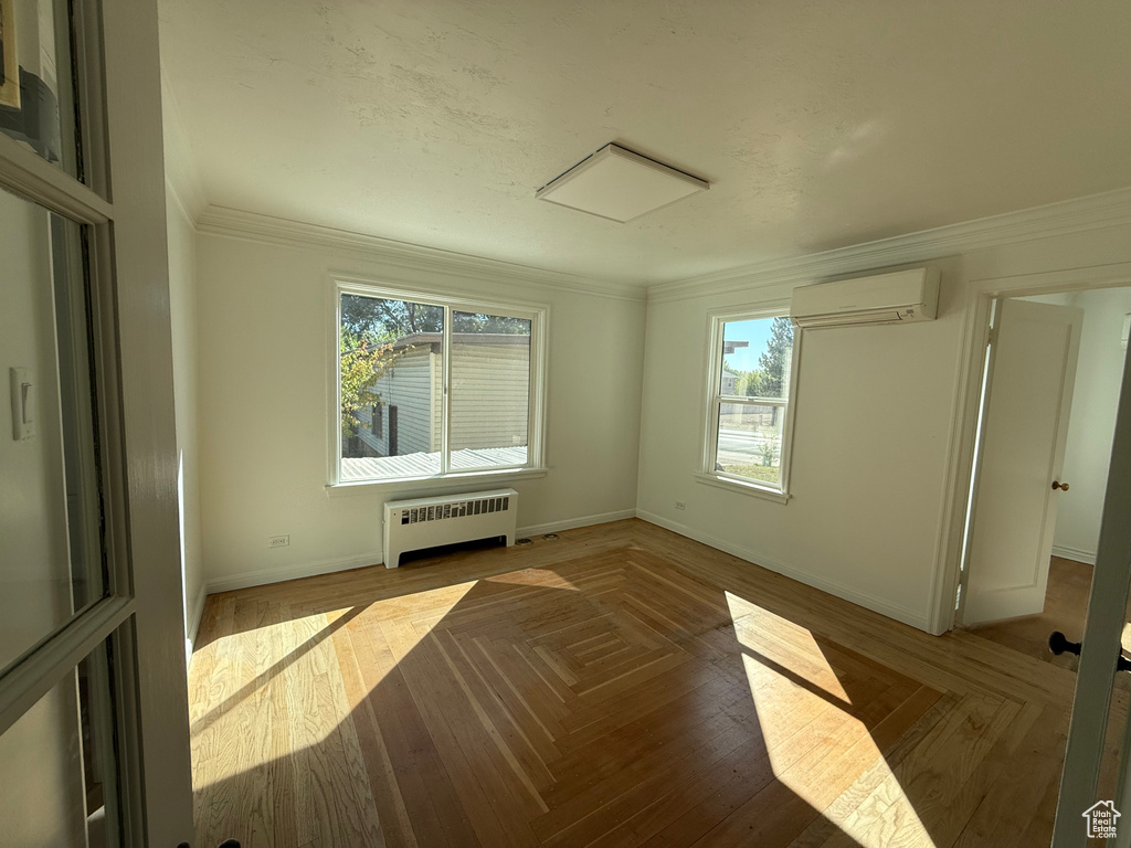 Empty room featuring a wealth of natural light, ornamental molding, a wall mounted air conditioner, and radiator