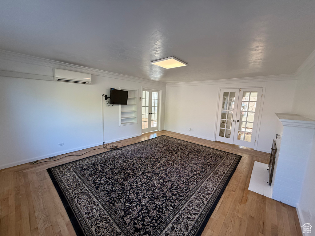 Empty room with ornamental molding, french doors, a wall unit AC, and light wood-type flooring