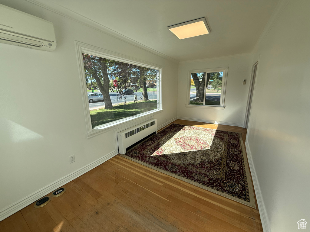 Interior space with a wall unit AC, wood-type flooring, radiator, and crown molding