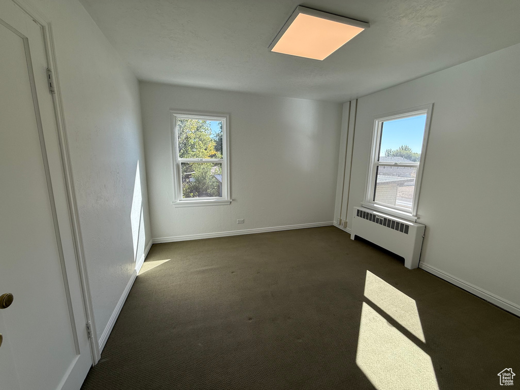 Empty room featuring radiator and dark colored carpet