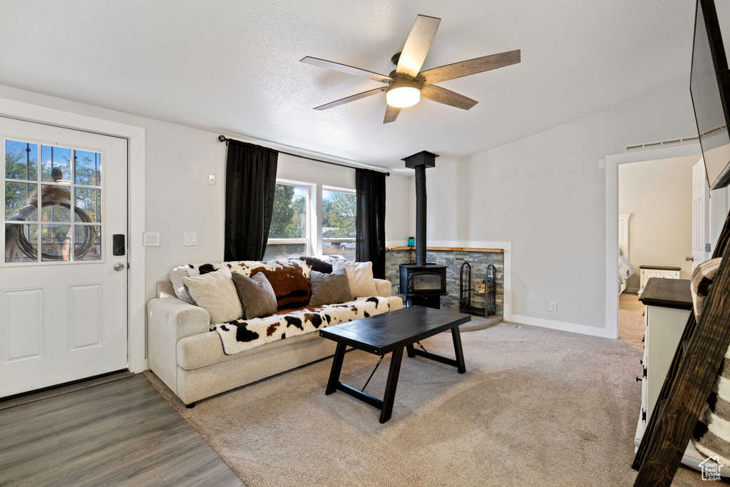 Living room featuring a textured ceiling, hardwood / wood-style flooring, a wood stove, and ceiling fan