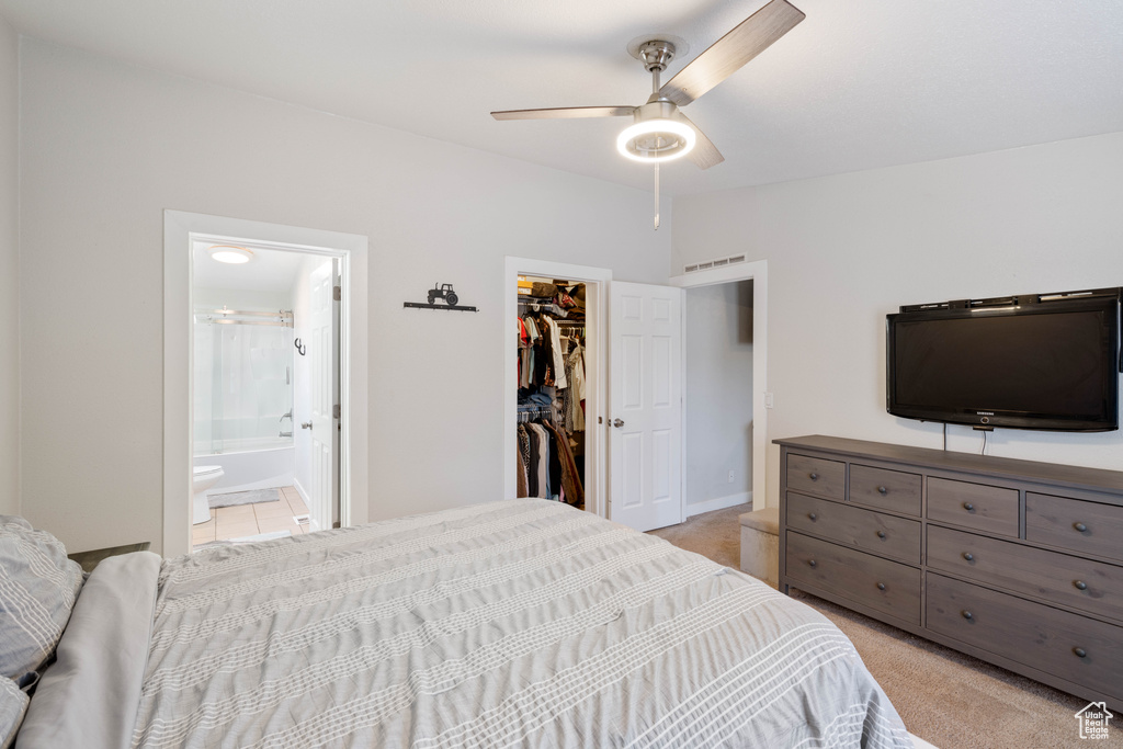 Carpeted bedroom with a spacious closet, a closet, ensuite bathroom, and ceiling fan