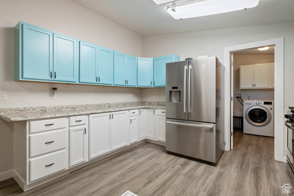 Kitchen featuring washer / dryer, blue cabinets, stainless steel appliances, vaulted ceiling, and light hardwood / wood-style flooring