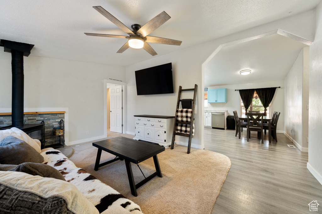 Living room with ceiling fan, lofted ceiling, a wood stove, and light hardwood / wood-style flooring