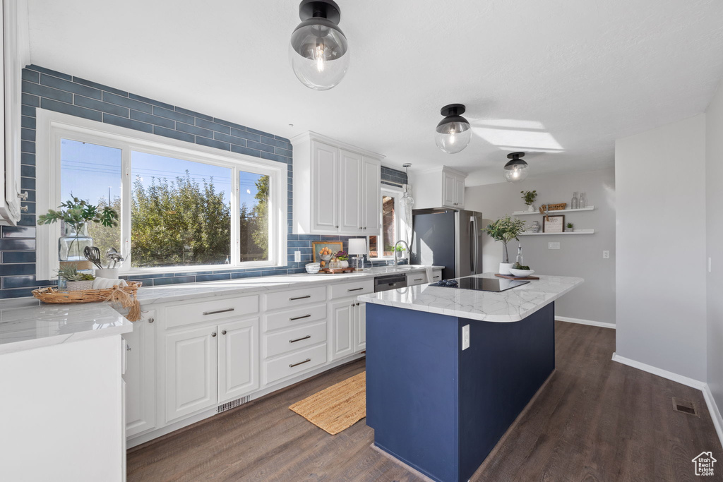 Kitchen with a kitchen island, stainless steel appliances, light stone countertops, white cabinetry, and dark hardwood / wood-style flooring