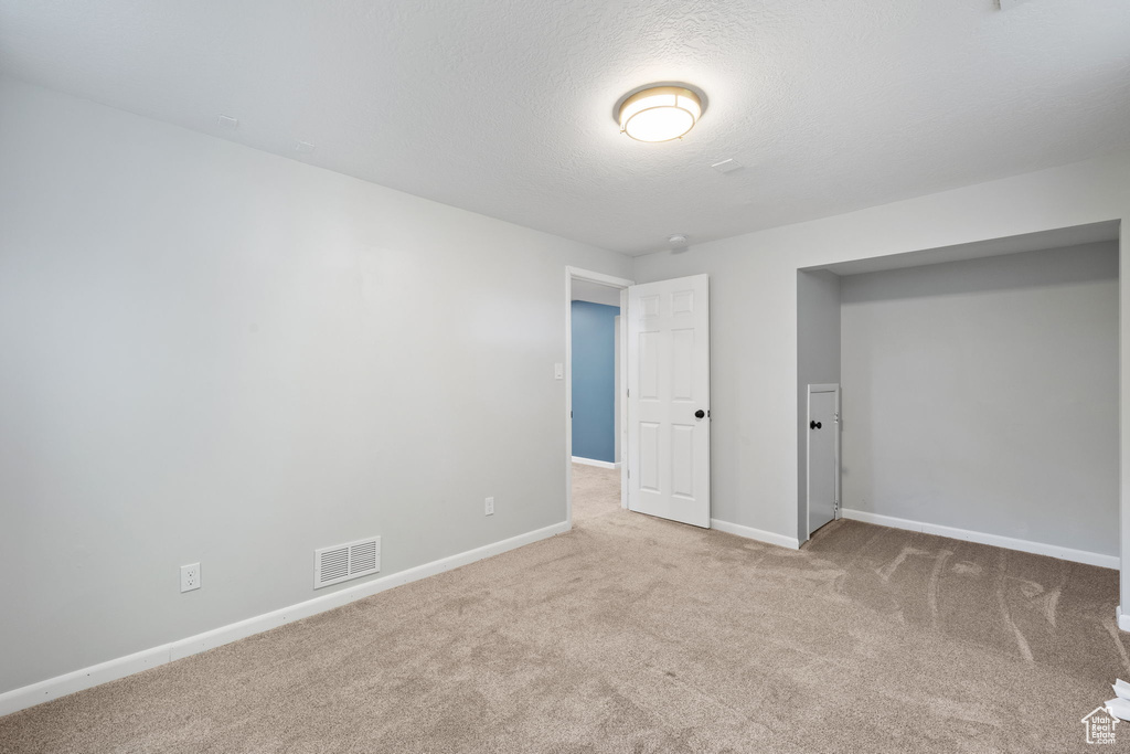 Unfurnished bedroom featuring a closet, light carpet, and a textured ceiling