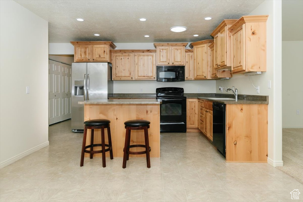 Kitchen with black appliances, recessed lighting, light brown cabinetry, a sink, and a breakfast bar