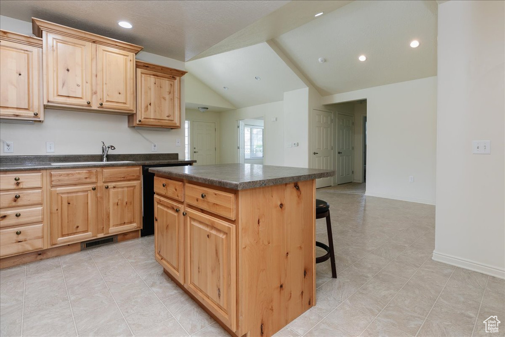 Kitchen featuring a sink, dark countertops, lofted ceiling, light brown cabinets, and a kitchen bar