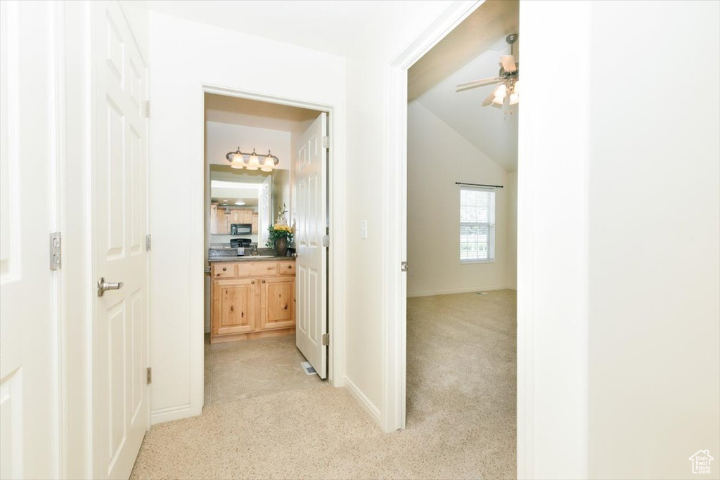 Hallway with light colored carpet, vaulted ceiling, and baseboards