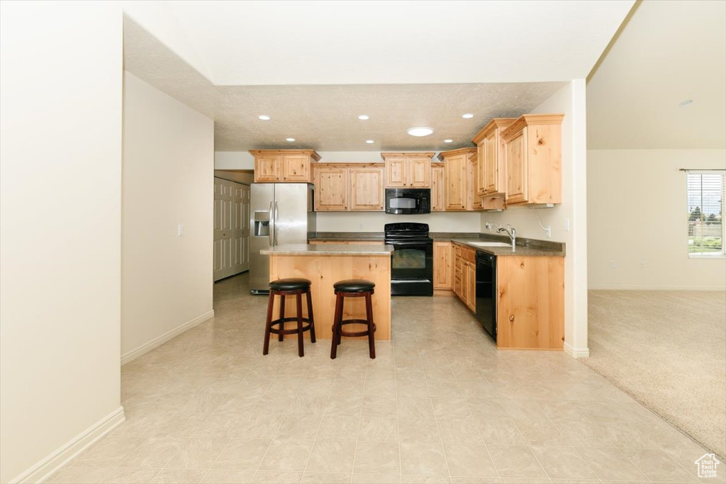 Kitchen with black appliances, light brown cabinets, recessed lighting, a kitchen breakfast bar, and a center island