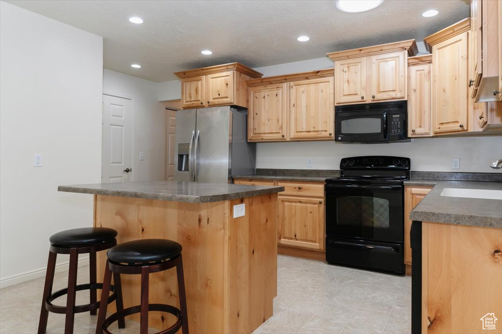 Kitchen with black appliances, light brown cabinets, dark countertops, a sink, and a kitchen island