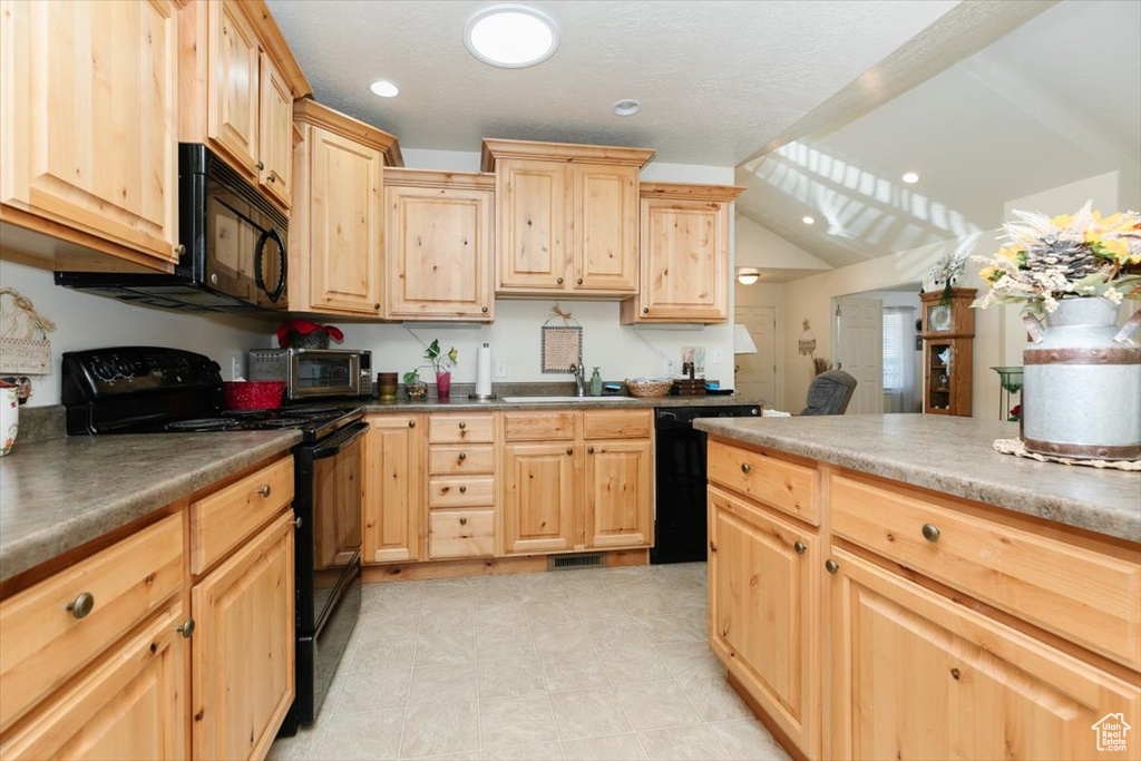 Kitchen featuring sink, black appliances, light brown cabinets, and lofted ceiling