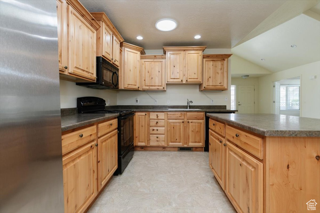 Kitchen with black appliances, dark countertops, light brown cabinets, lofted ceiling, and a sink