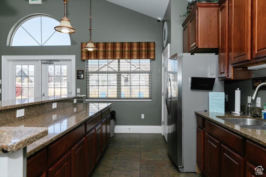 Kitchen with hanging light fixtures, stainless steel fridge, sink, vaulted ceiling, and light stone counters