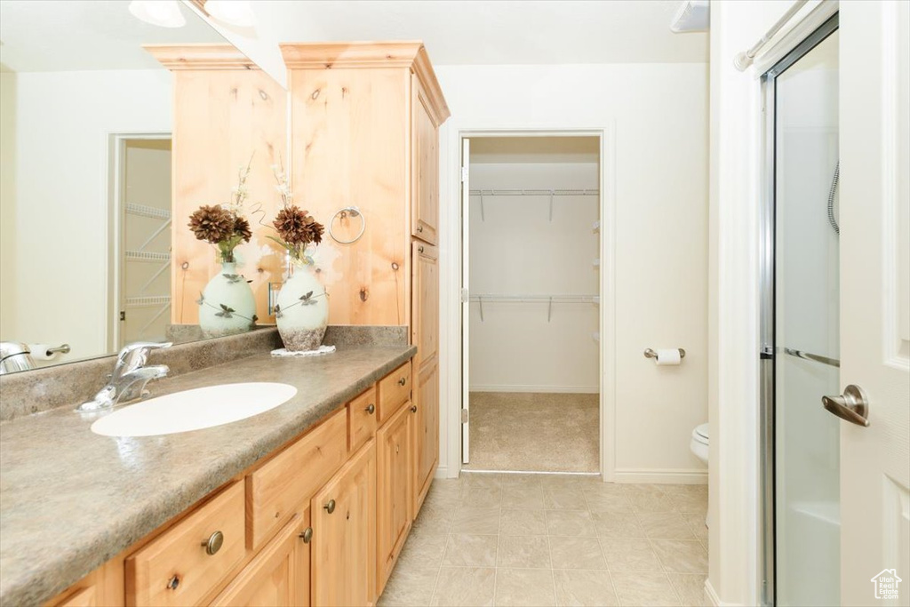 Bathroom featuring vanity, a walk in closet, toilet, baseboards, and a shower with shower door