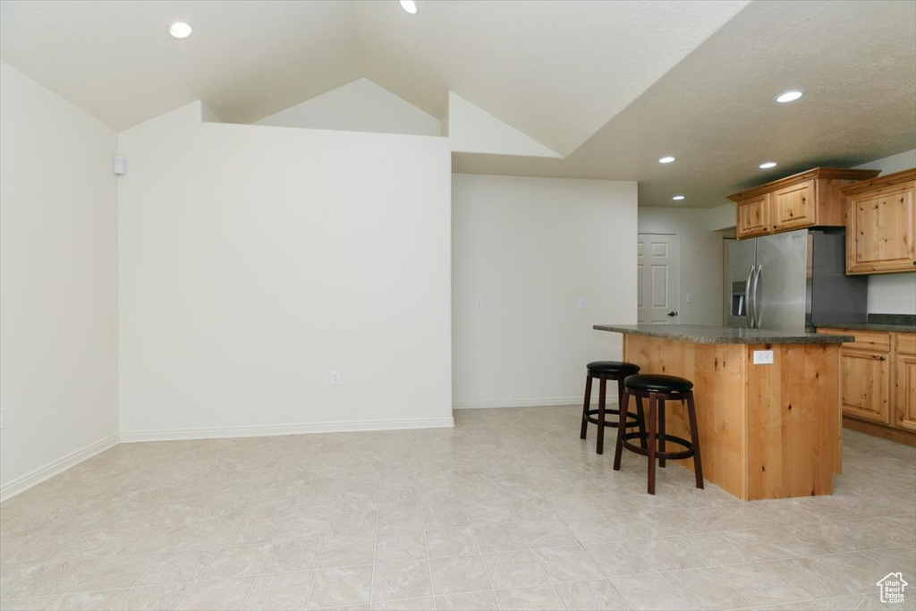 Kitchen featuring stainless steel refrigerator with ice dispenser, a kitchen bar, lofted ceiling, a center island, and recessed lighting