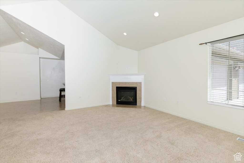 Unfurnished living room featuring lofted ceiling, light colored carpet, recessed lighting, a fireplace with flush hearth, and baseboards