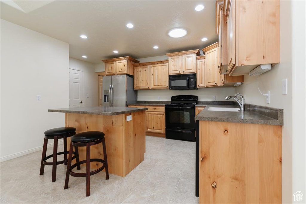 Kitchen with black appliances, a sink, dark countertops, a center island, and a breakfast bar area