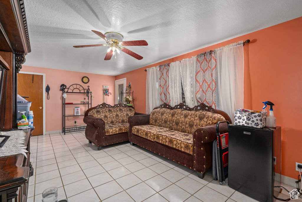 Living room with a textured ceiling, light tile patterned floors, and ceiling fan