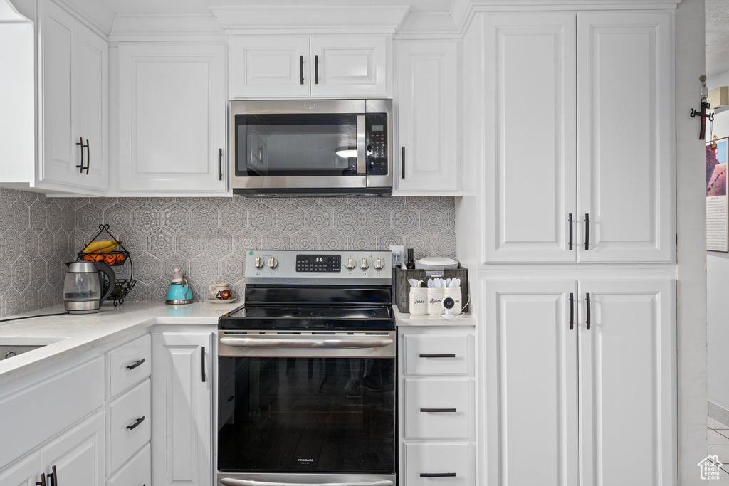 Kitchen featuring backsplash, appliances with stainless steel finishes, and white cabinets