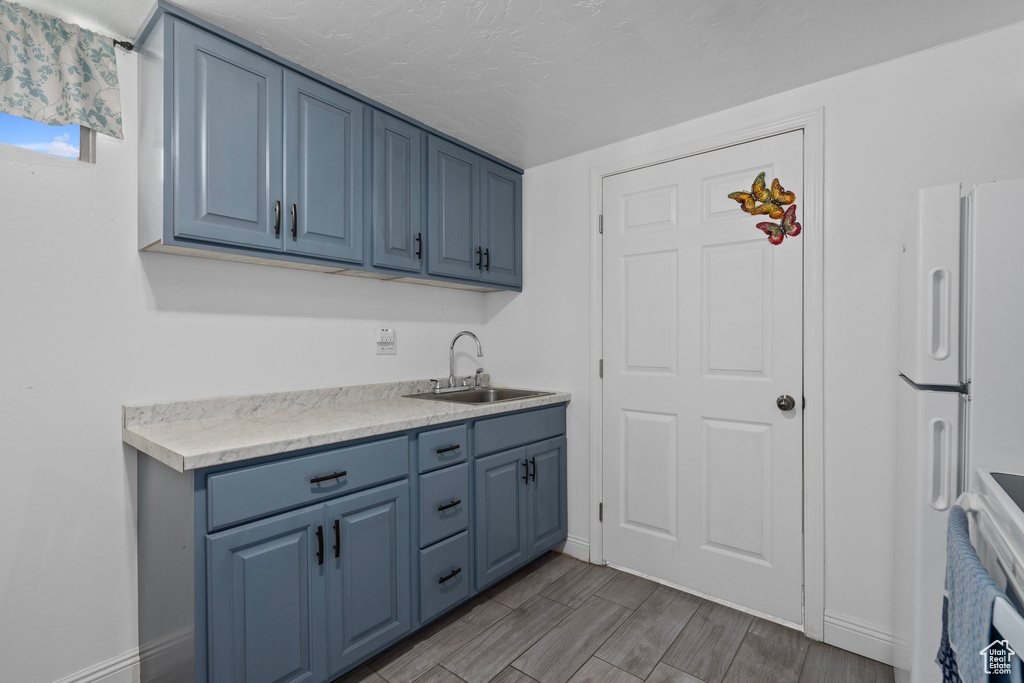 Kitchen with blue cabinetry, sink, light hardwood / wood-style flooring, and white refrigerator