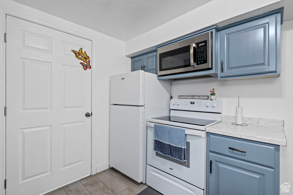 Kitchen with light hardwood / wood-style floors, white refrigerator, blue cabinetry, and electric range oven