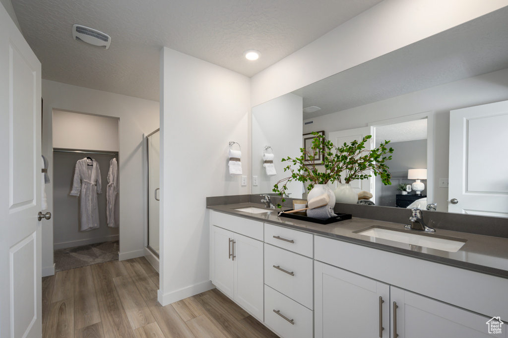 Bathroom featuring vanity, hardwood / wood-style floors, a shower with shower door, and a textured ceiling