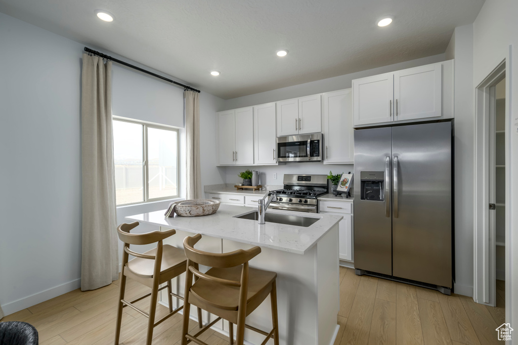 Kitchen with a center island with sink, light stone counters, white cabinetry, light hardwood / wood-style floors, and stainless steel appliances